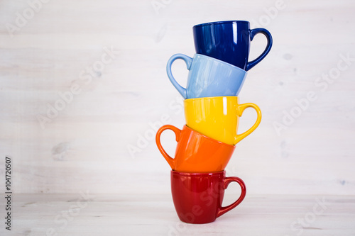 a stack of colorful coffee cups on a white wooden background
