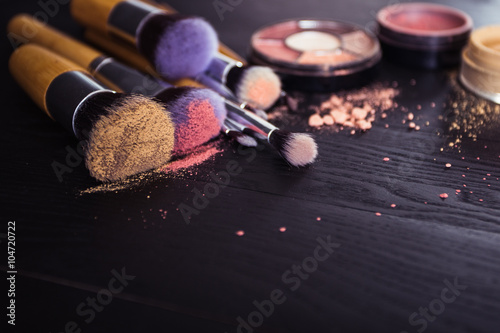 make up brushes with powder and rouge on a black wooden background