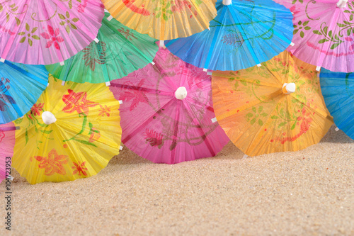 Colorful paper cocktail umbrellas in sand