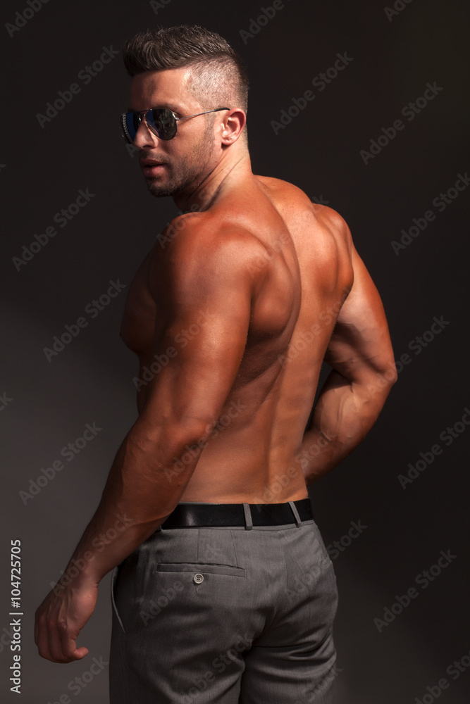 shirtless muscular man in pants and sunglasses posing in studio