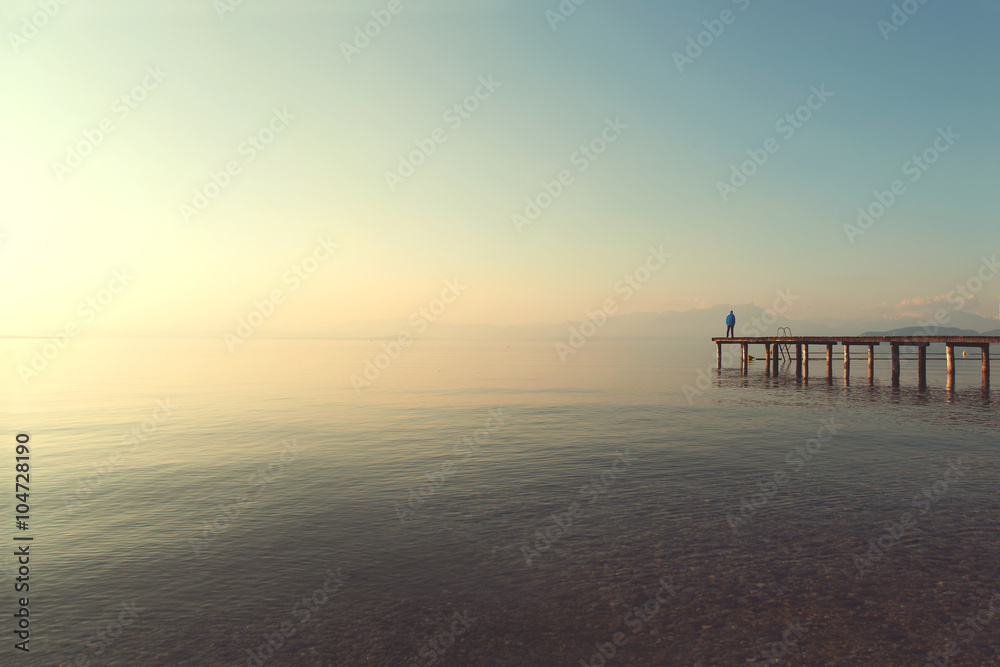 man on a boardwalk observing calm lake scenary at sunset