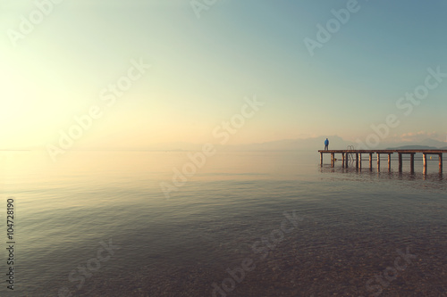 man on a boardwalk observing calm lake scenary at sunset © fran_kie