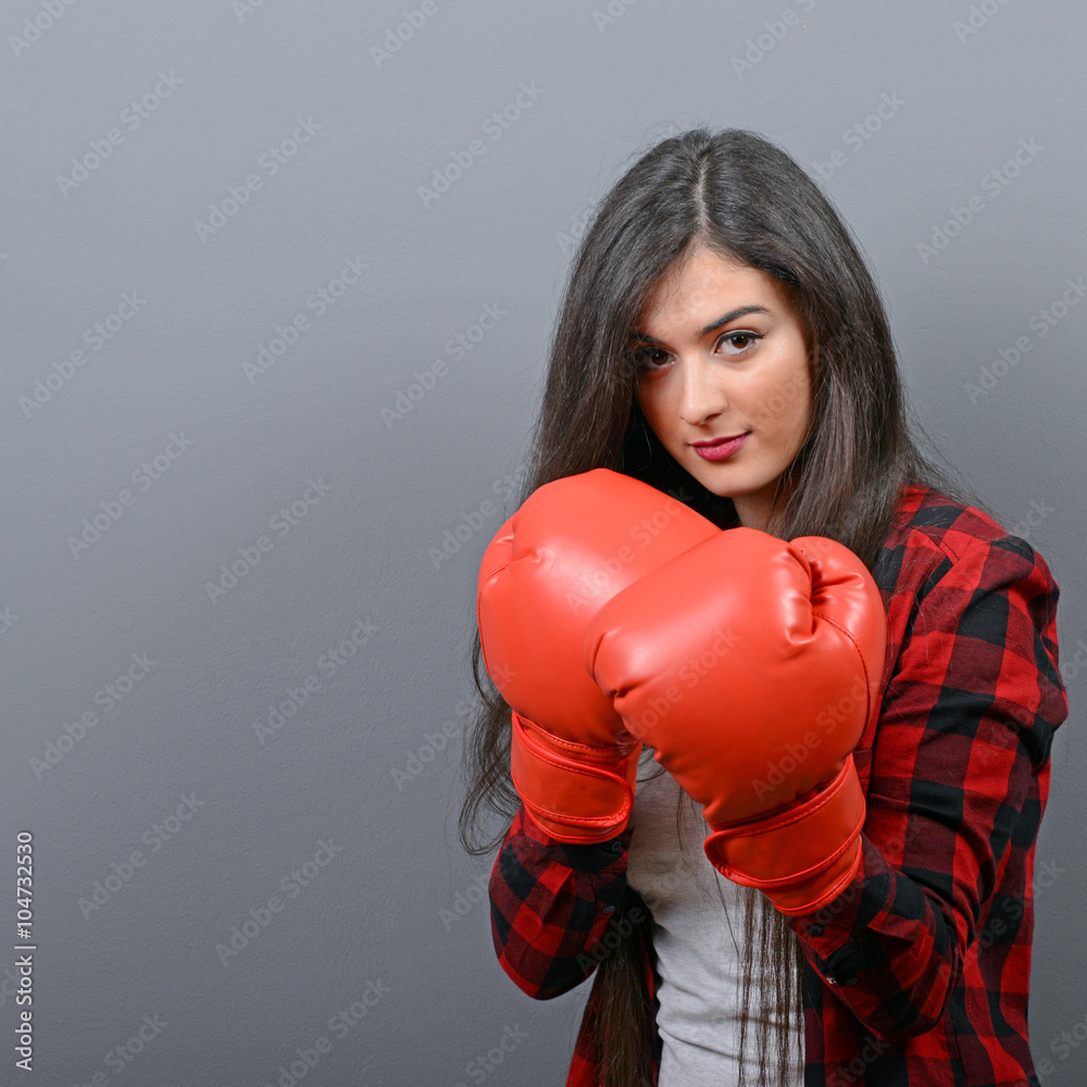 Portrait of young woman posing with boxing gloves against gray b Portrait of young woman posing with boxing gloves against gray b