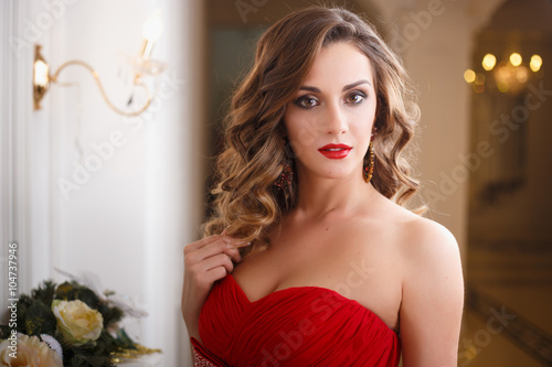 Beautiful young woman with perfect make up and hair style in gorgeous red evening dress in expensive luxury interior photo