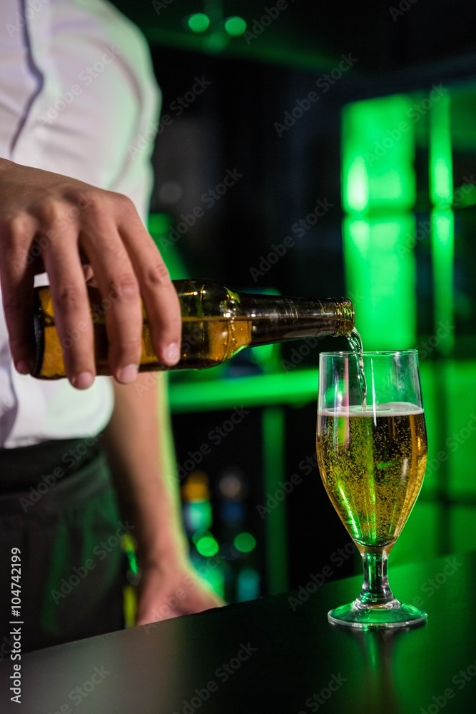 Mid section of bartender pouring beer in a glass