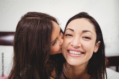 Daughter kissing mother on bed at home