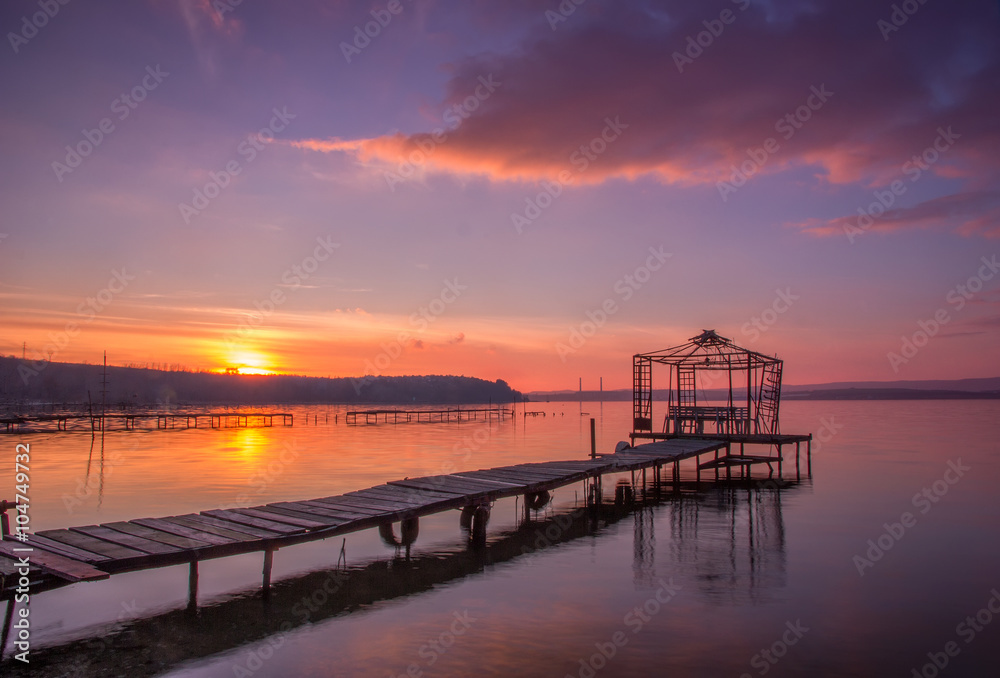 Sunset on the bay with old wooden bridge pier with gazebo
