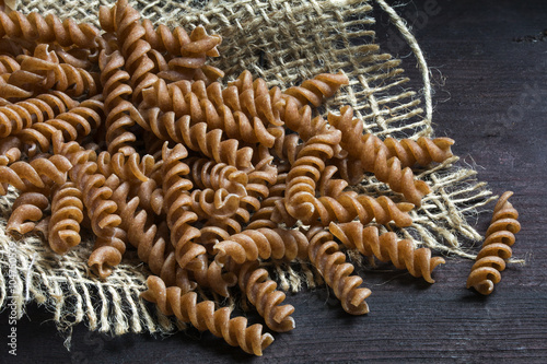 wholemeal pasta fusilli from organic spelt on burlap and dark wood