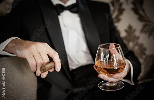Foto Gentleman holding glass of cognac and cigar