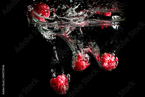 Raspberries splashing into water on black background.