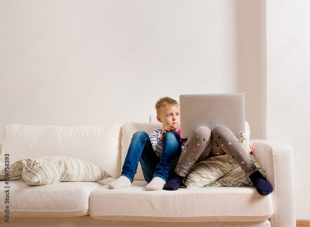 Children at home sitting on sofa, playing with laptop Children at home sitting on sofa, playing with laptop