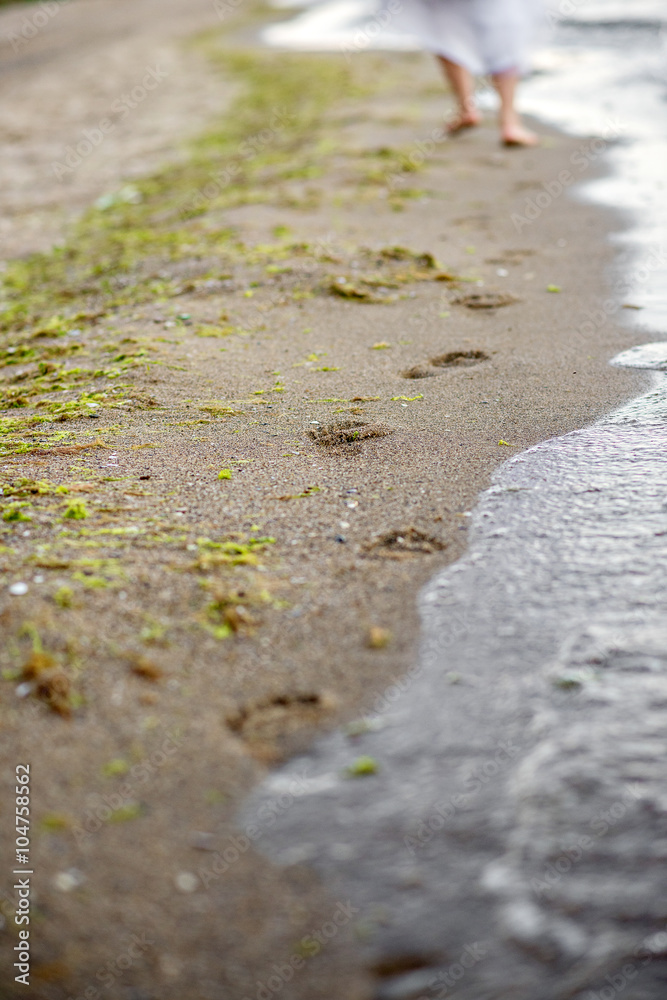 The girl in a white dress running down the beach, leaving footprints in the sand The girl in a white dress running down the beach, leaving footprints in the sand