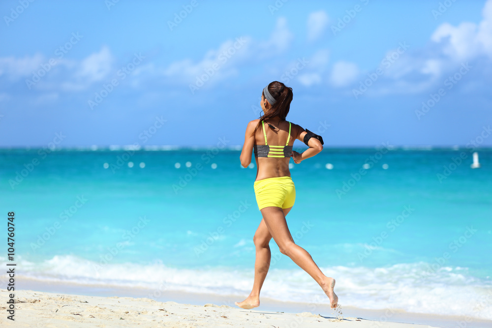 Running on beach - summer workout active lifestyle. Female athlete from the back running away barefoot on the sand in trendy activewear outfit training cardio for weight loss.