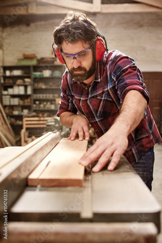 Carpenter wearing protective gear cutting a plank of wood