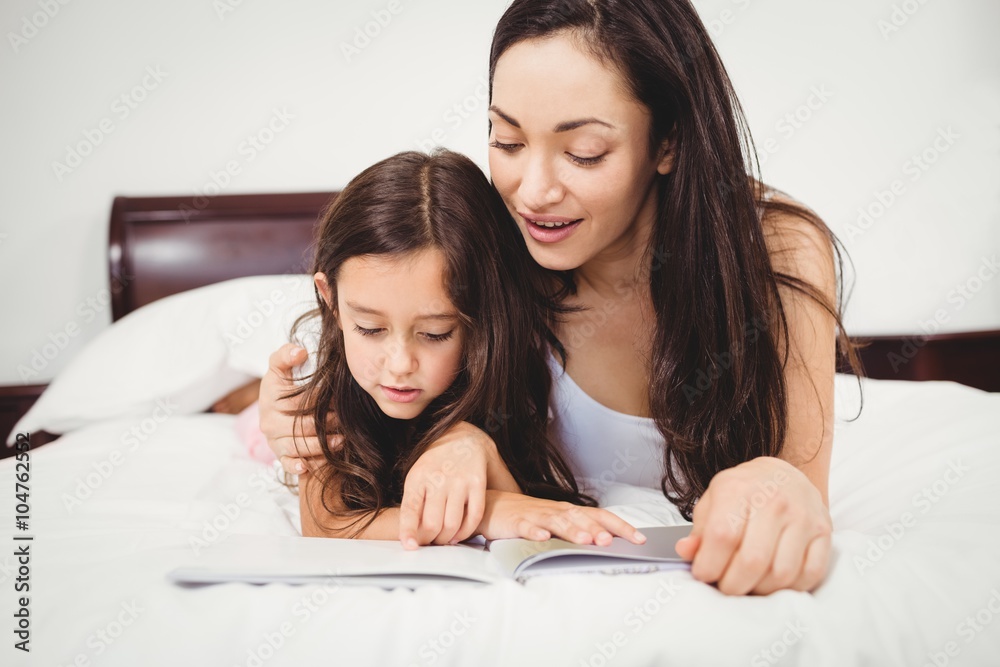Daughter reading book with mother on bed Daughter reading book with mother on bed