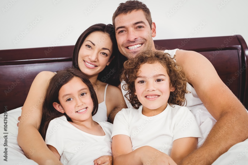Cheerful family lying on bed against wall at home Cheerful family lying on bed against wall at home