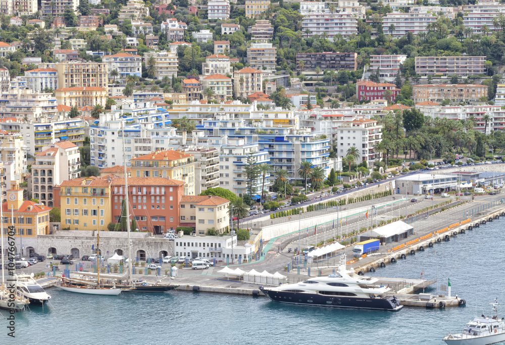 Cityscape of French Mediterranean sea port of Nice with super yachts, sail boats mooring in the harbor, villas with tropical gardens and apartments on the hill