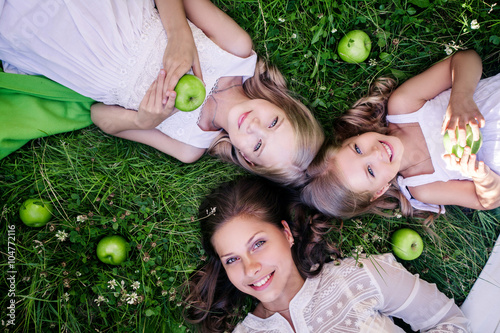 Mother and daughters lying on green grase. Happy family outdoors