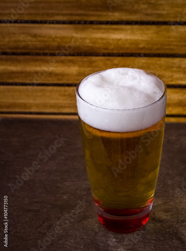 Glass full of beer on flat base and wooden background 