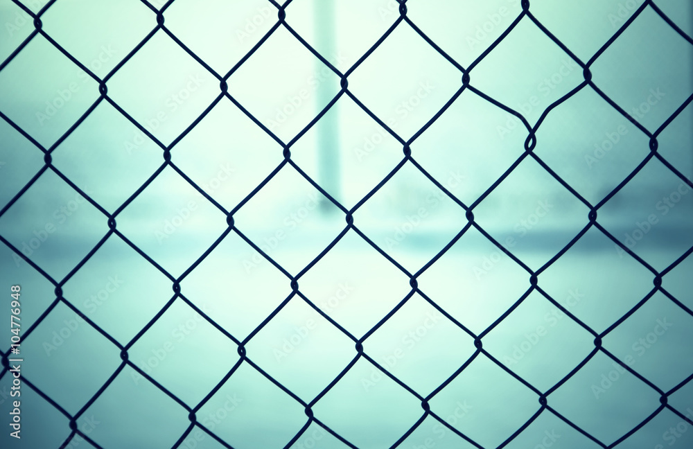 Fototapeta premium Outside abstract wire fence closeup with bright blue blurred background. 