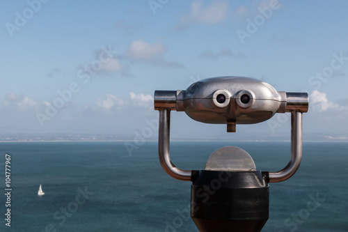 Sightseeing binoculars overlooking ocean with a sailboat in the distance.