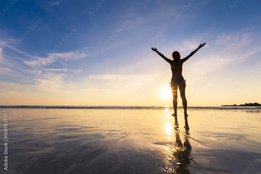 Young happy woman raising hands on a beautiful beach, sunset