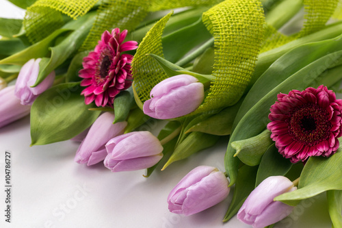 Wiosenny pastelowy bukiet z liliowych tulipanów i różowych gerber na białym tle z jutową jasnozieloną taśmą ozdobną