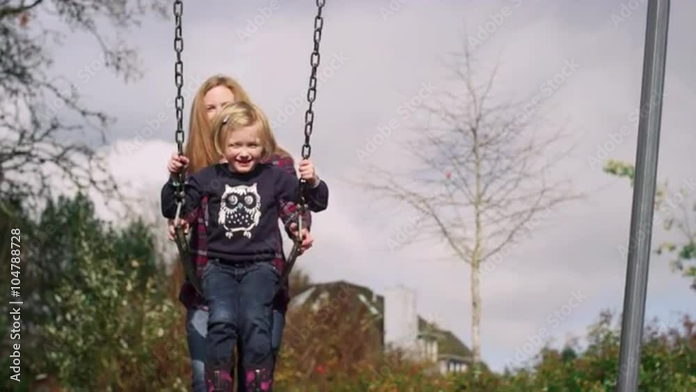 A mother pushing her daughter on a swing at the park, slow motion A mother pushing her daughter on a swing at the park, slow motion