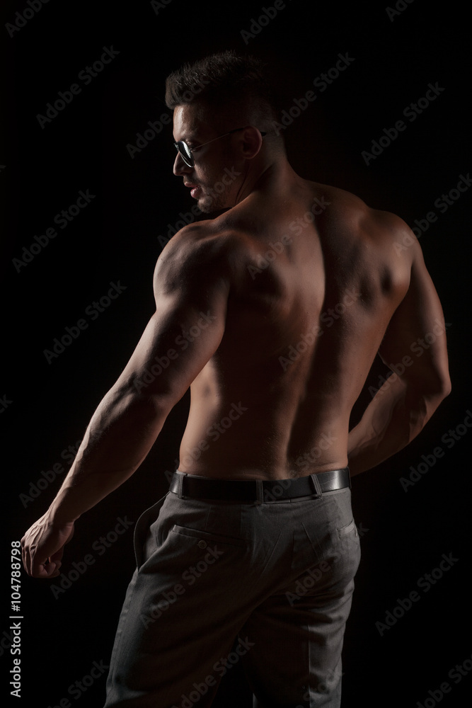 back view of naked muscular man in pants on black