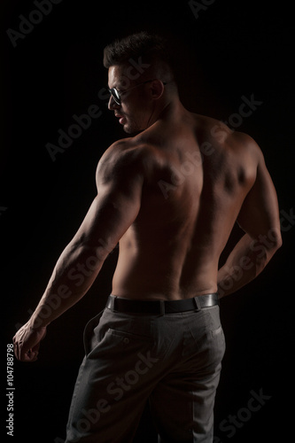 back view of naked muscular man in pants on black