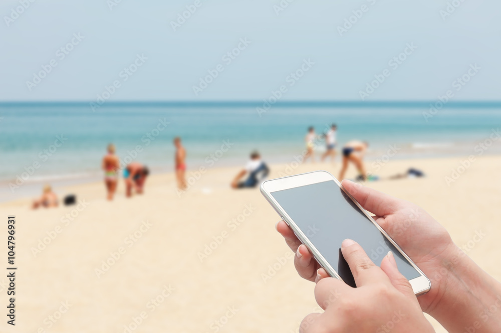 Naklejka premium Women using smartphone top on blurred blue sea and white sand be