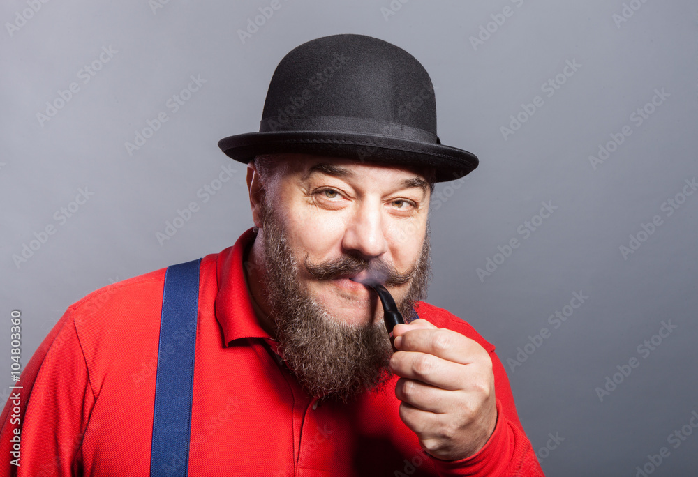 An elderly man in a bowler hat with a beard smokes a pipe 
