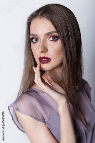 Portrait of a beautiful girl with a sweet delicate burgundy lips and bright makeup in a light transparent negligee studio on a white background