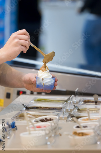 Woman prepares and serves a frozen yogurt with caramel