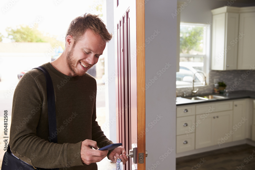 Man Checking Mobile Phone As He Opens Door Of Apartment