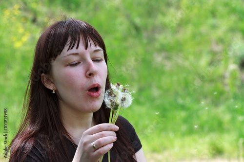 Young adult woman is blowing dandelion on green background.