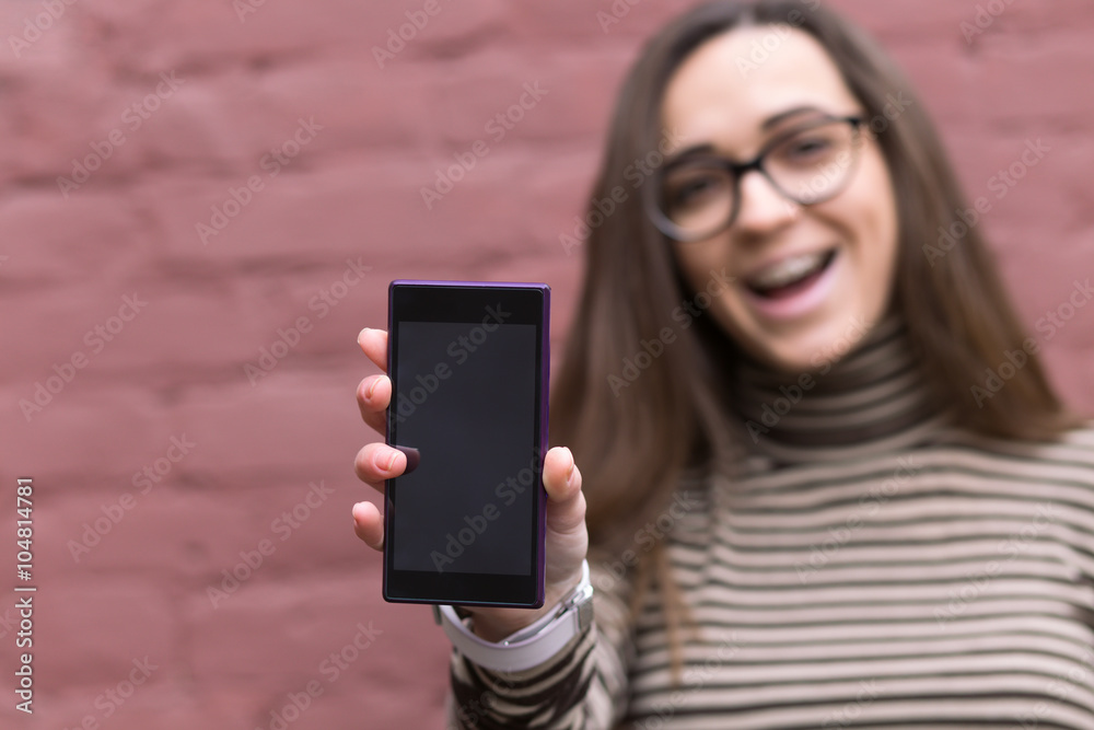 Woman standing against a brick wall background and holding up her mobile phone