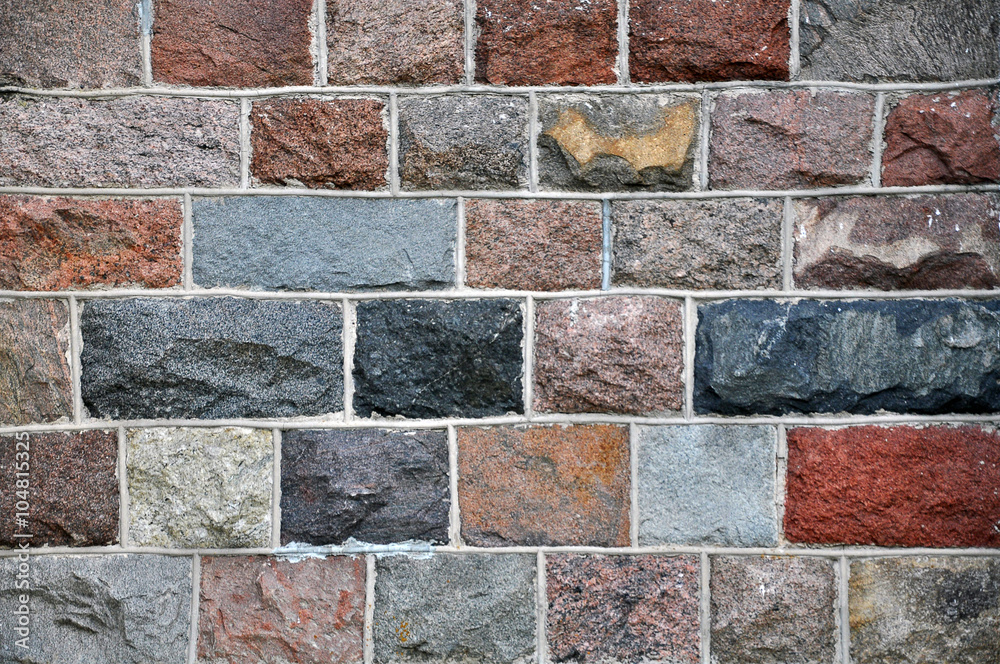 Wall built of rectangular bricks made of natural stone of different colors.