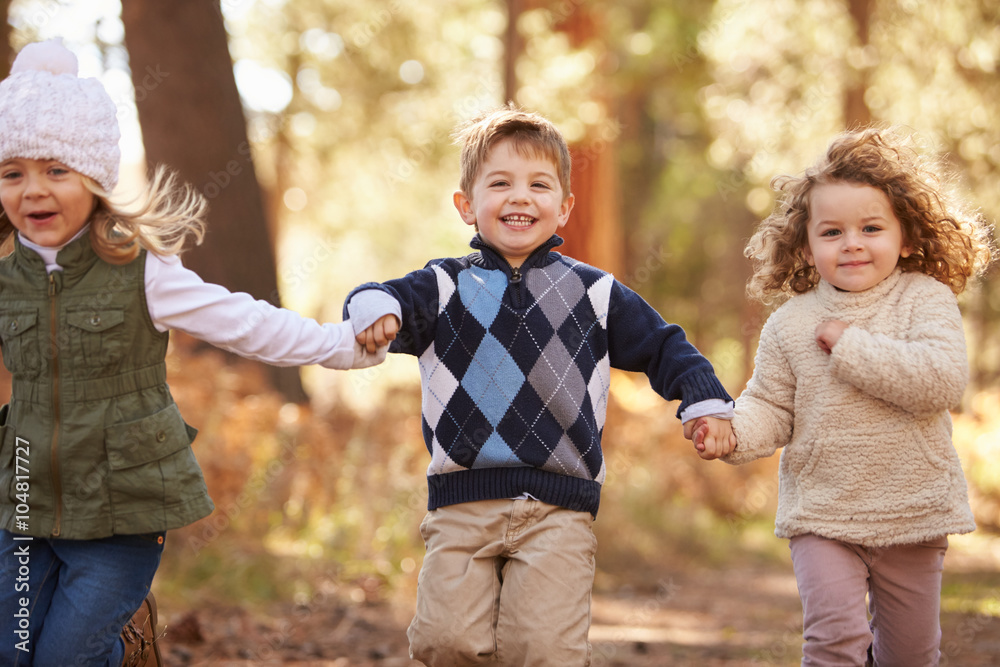 Group Of Young Children Running Along Path In Autumn Forest