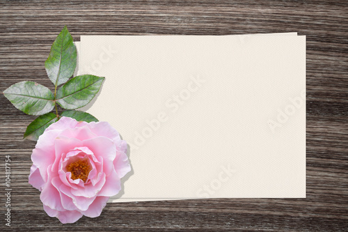 Pink rose and and paper on wood background