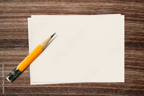 Yellow pencil and paper on wood background