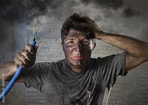 young man holding cable smoking after electrical accident with dirty burnt face in funny sad expression