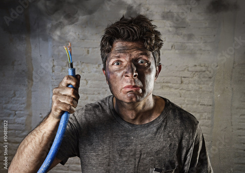 young man holding  cable smoking after electrical accident with dirty burnt face in funny sad expression