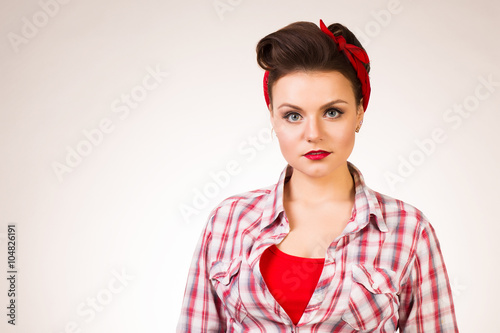 Beautiful young woman with pin-up make-up and hairstyle posing over pink background