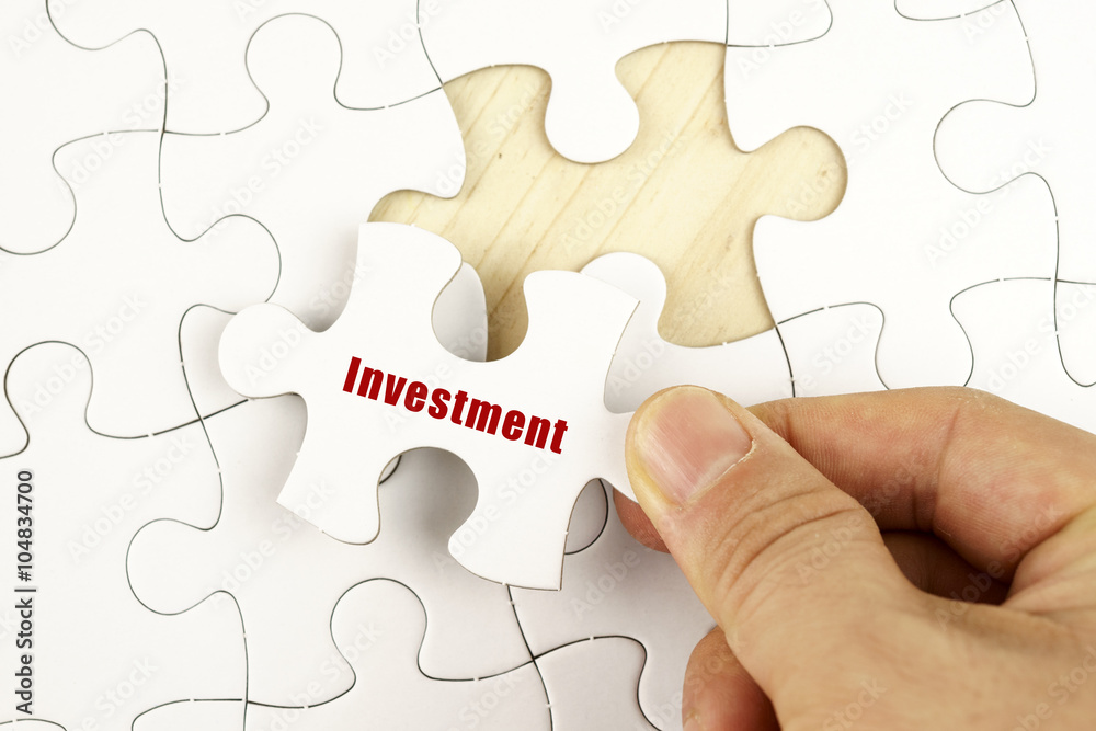 Fototapeta premium Finance concept. Hand holding piece of jigsaw puzzle showing INVESTMENT word.