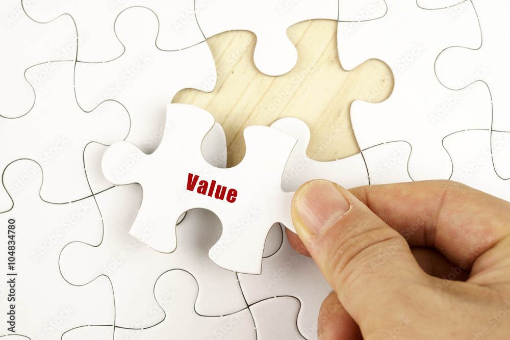 Fototapeta premium Finance concept. Hand holding piece of jigsaw puzzle showing VALUE word.