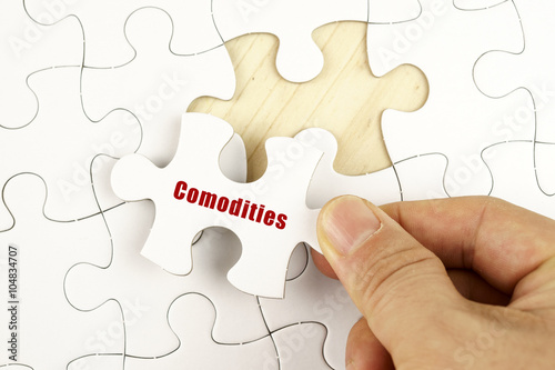 Finance concept. Hand holding piece of jigsaw puzzle showing COMODITIES word. photo