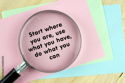 Magnifying glass on papers with word quote of "Start where your are,use what you have,do what you can" written on it.