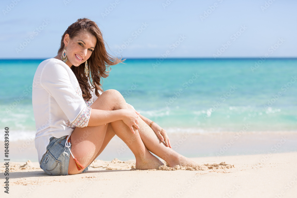 Junge hübsche Frau in Jeans Hot Pants sitzt am Strand vor blauem Ozean Junge hübsche Frau in Jeans Hot Pants sitzt am Strand vor blauem Ozean