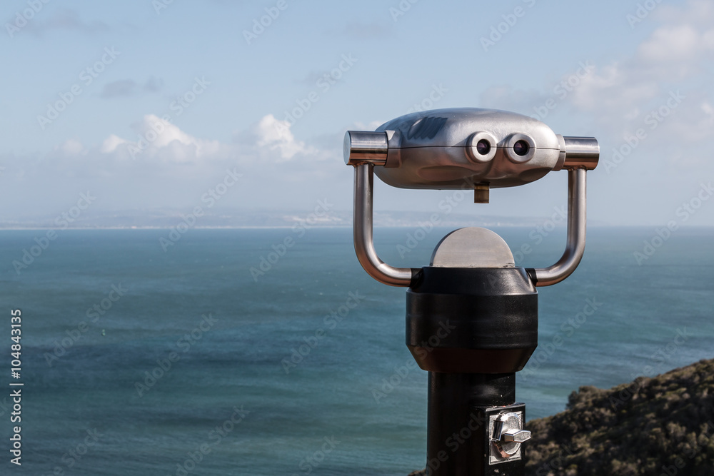 Sightseeing binoculars high on mountain overlooking ocean view.